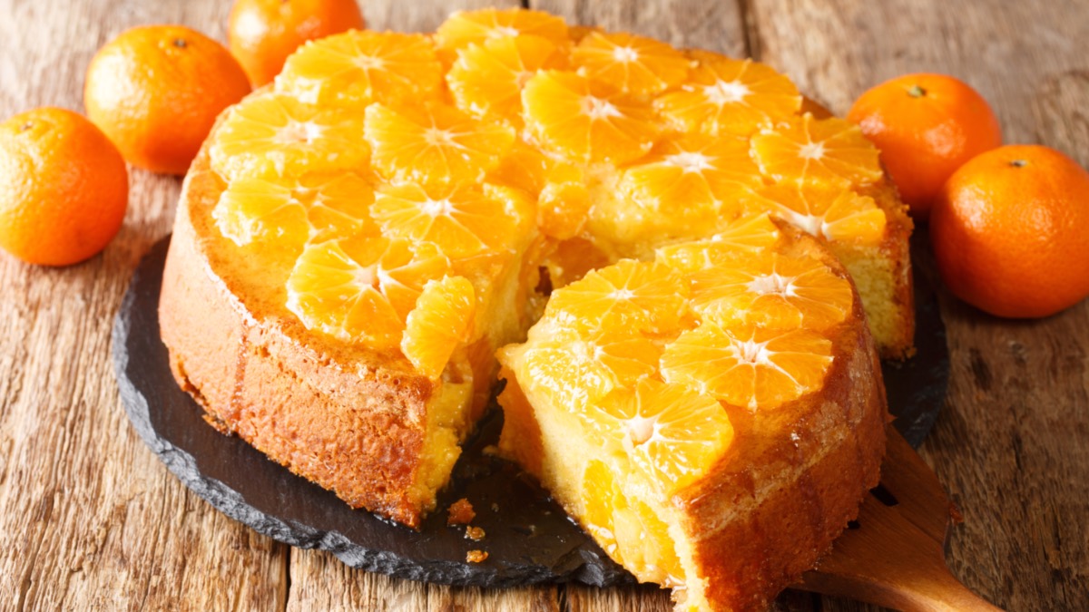 Ein Schüttelkuchen mit Mandarine. Ein großes Stück wurde herausgeschnitten und liegt vor dem Kuchen.