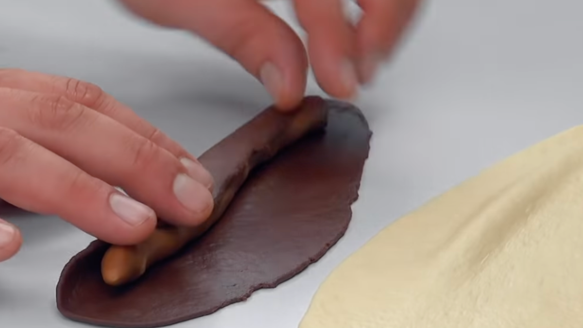 Flache Teigrolle wird um die schlangenförmige Teigrolle gewickelt