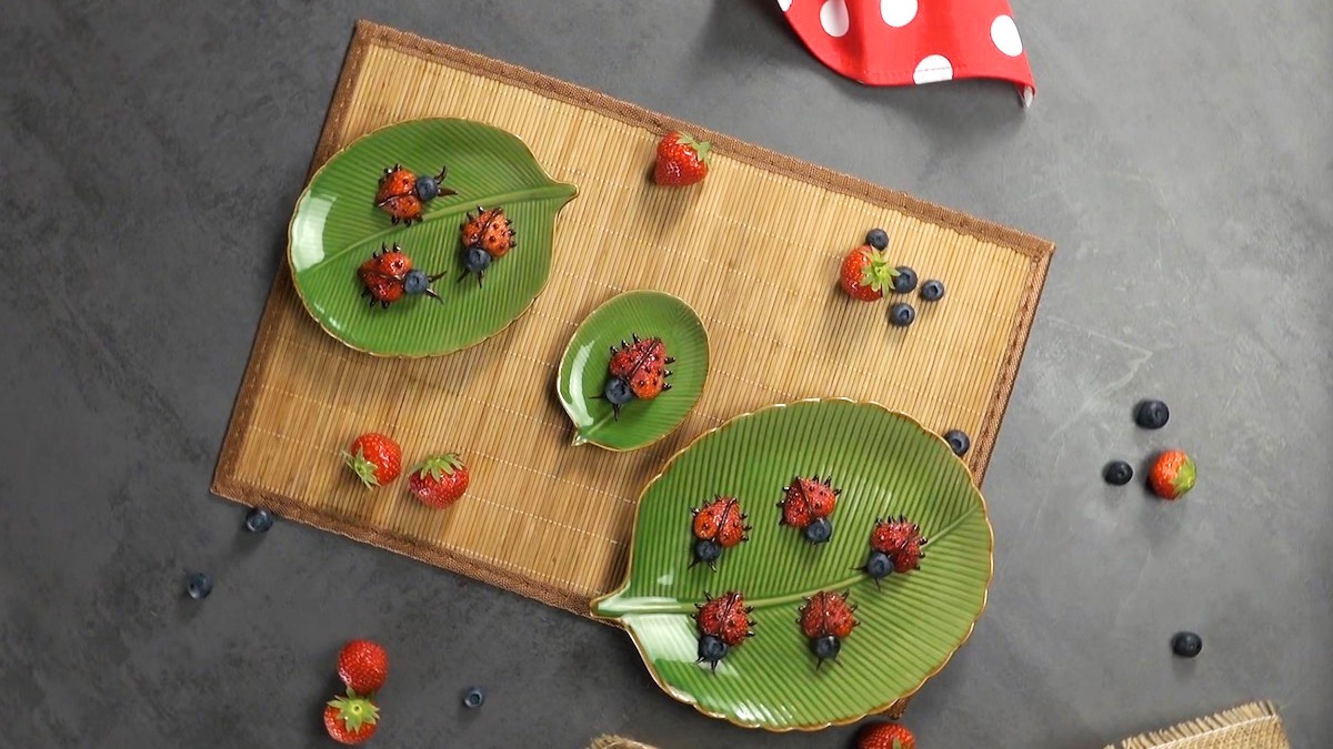 Tricks mit Erdbeeren: süße Marienkäfer aus Erdbeeren auf Tellern in der Draufsicht.