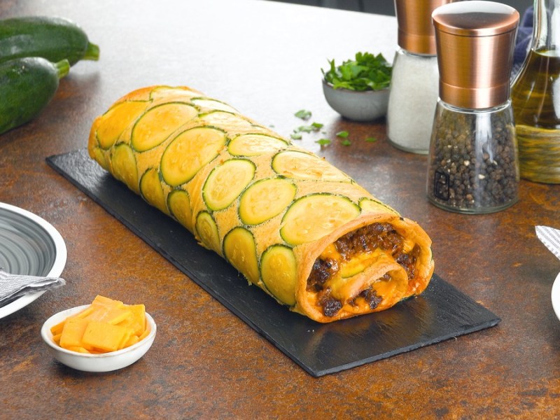 Zucchini-Hackfleisch-Rolle mit Cheddar auf einem schwarzen Brett serviert.