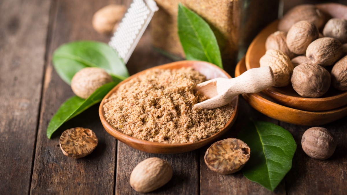 Gemahlene Muskatnuss in Schüssel neben halbierten und intakten Nüssen