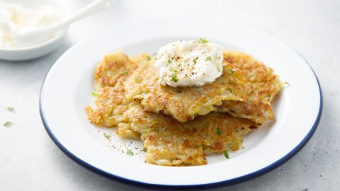 Ein Stapel Pastinaken-Kartoffel-Puffer mit Kräuter-Dip auf einem weißen Teller. Im Hintergrund eine Schale mit Dip.