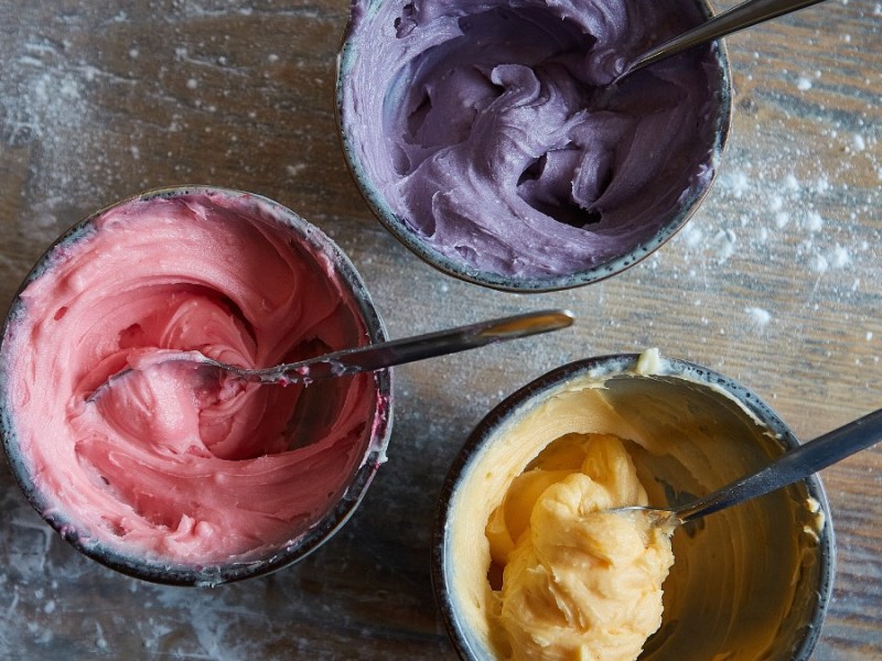 3 Schüssel mit verschieden farbigen Teigen. Einer in lila, einer in rosa und einer in gelb.
