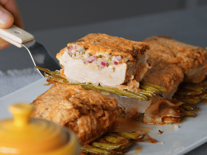 Schweinefilet Strindberg, aus dem ein Stück herausgehoben iwrd, mit Soße und Speckbohnen.