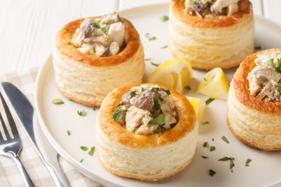 4 Blätterteig-Pasteten mit Pilzen auf einem Teller, daneben Messer und Gabel.