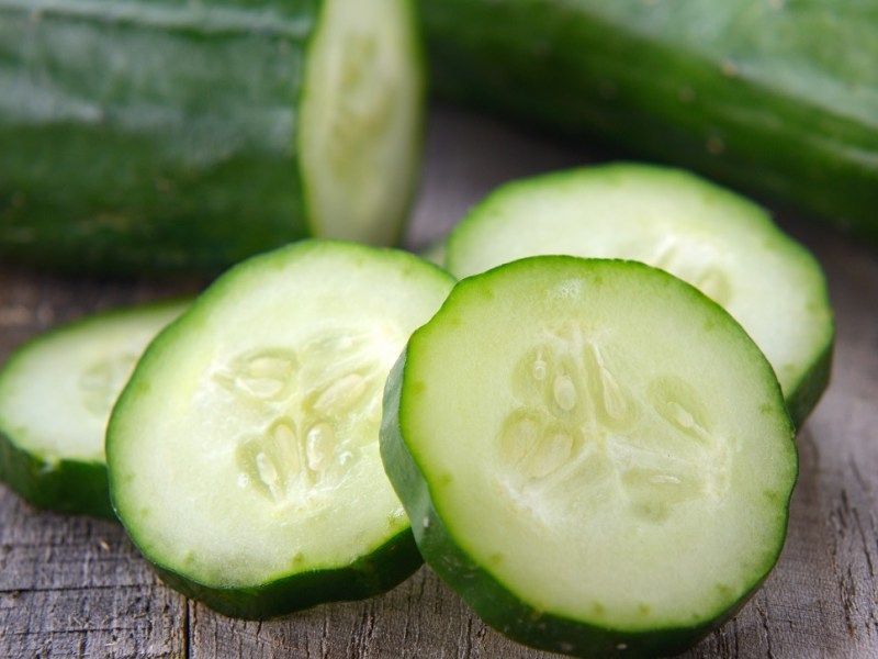 Einige Scheiben Gurke, die vor zwei Gurken liegen.