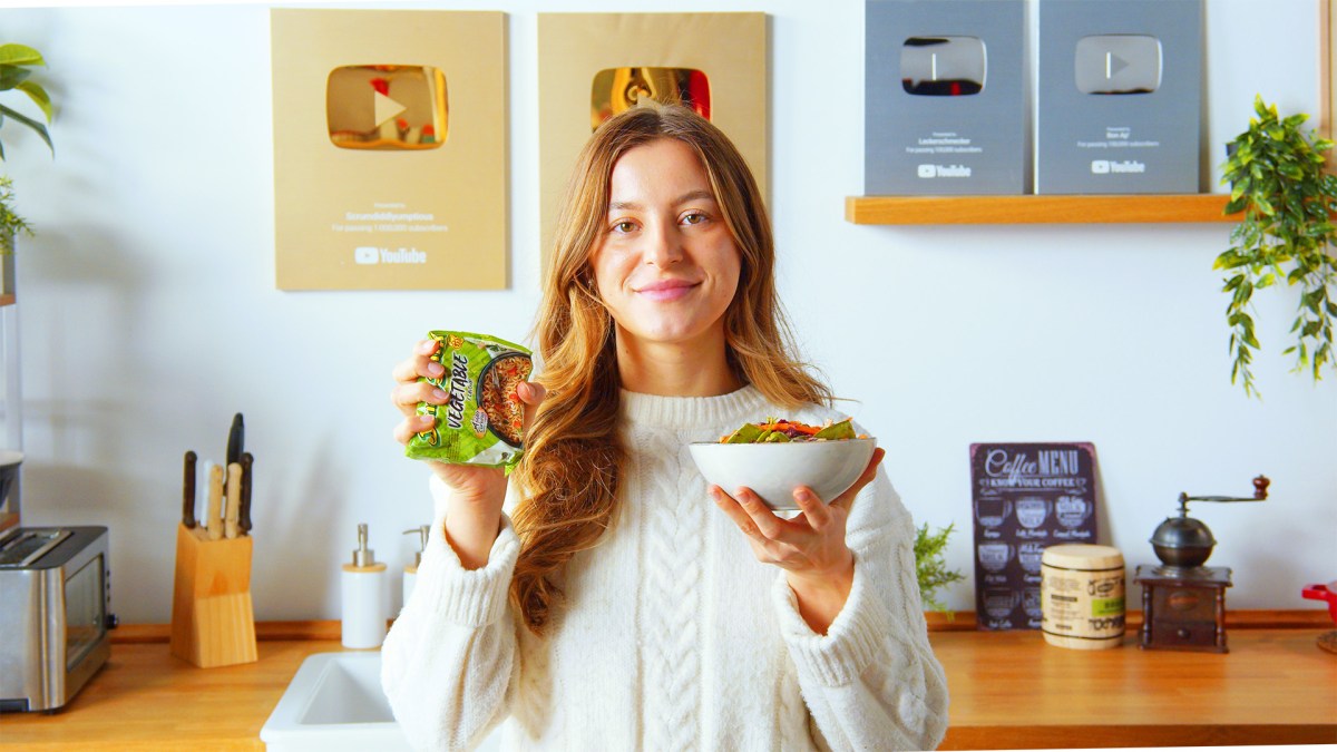 Eine Köchin hält eine Schale knuspriger Ramen-Salat und eine Packung Instant-Nudeln in die Kamera.
