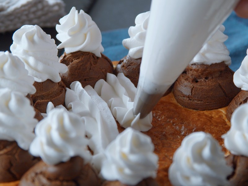 Windbeutel-Blätterteig-Kuchen, auf den Sahne gespritzt wird.