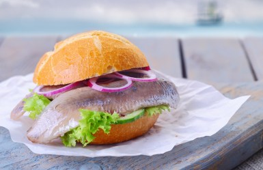 Matjesbrötchen auf einem Papier, das auf einem Holzbrett liegt.