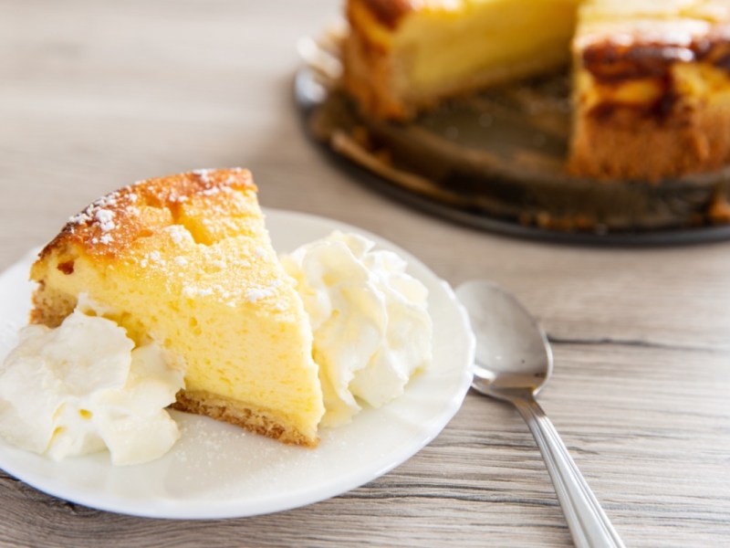 Tipps für Käsekuchen: Ein Stück Quarkkuchen mit Sahne auf einem Teller.