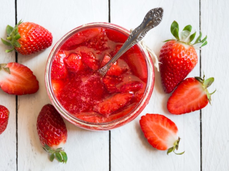 Wie bleibt Erdbeermarmekade rot: Erdbeermarmelade im Glas in der Draufsicht. Daneben frische Erdbeeren.