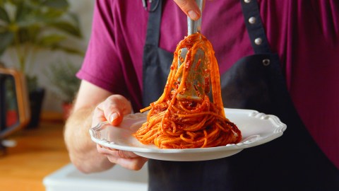 Ein Koche legt eine Potrion Spaghetti all'Assassina auf einen weißen Teller.