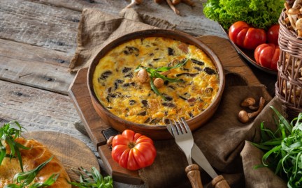 Eine Kartoffel-Frittata mit Pilzen in einer Pfanne. Drumherum liegen frische Zutaten.