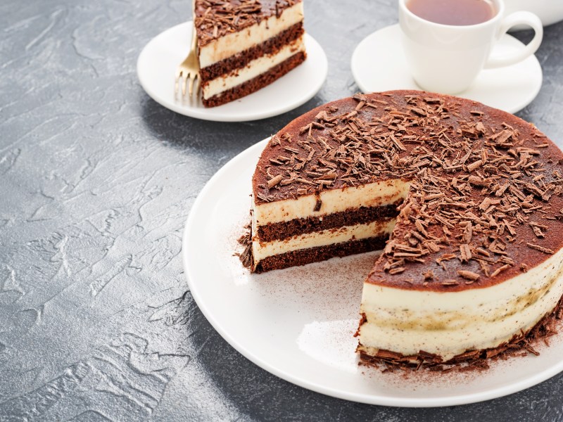 Eine Eierlikör-Tiramisu-Torte, von der ein Stück abgenommen wurde. Daneben steht eine Tasse Kaffee.