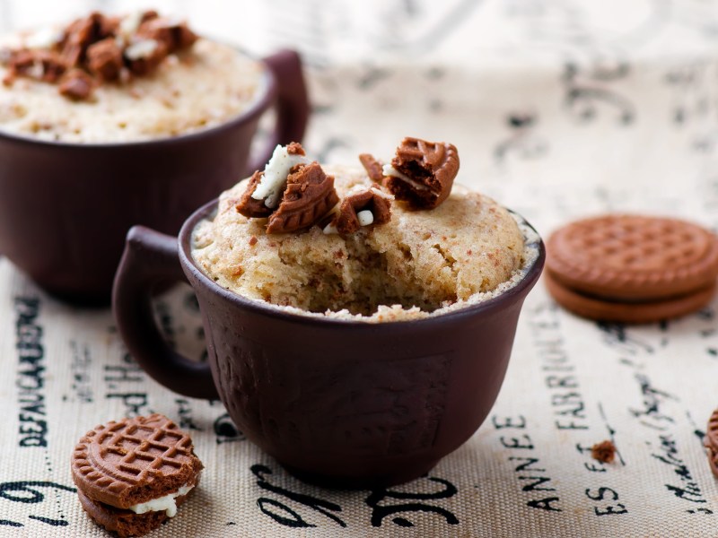 2 Tassen Lotus-Tassenkuchen garniert mit Kekskrümeln, drumherum einige Kekse.