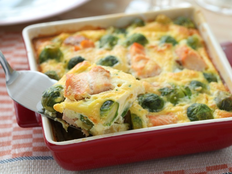 Rosenkohlauflauf mit Lachs und Kartoffeln in roter Auflaufform.