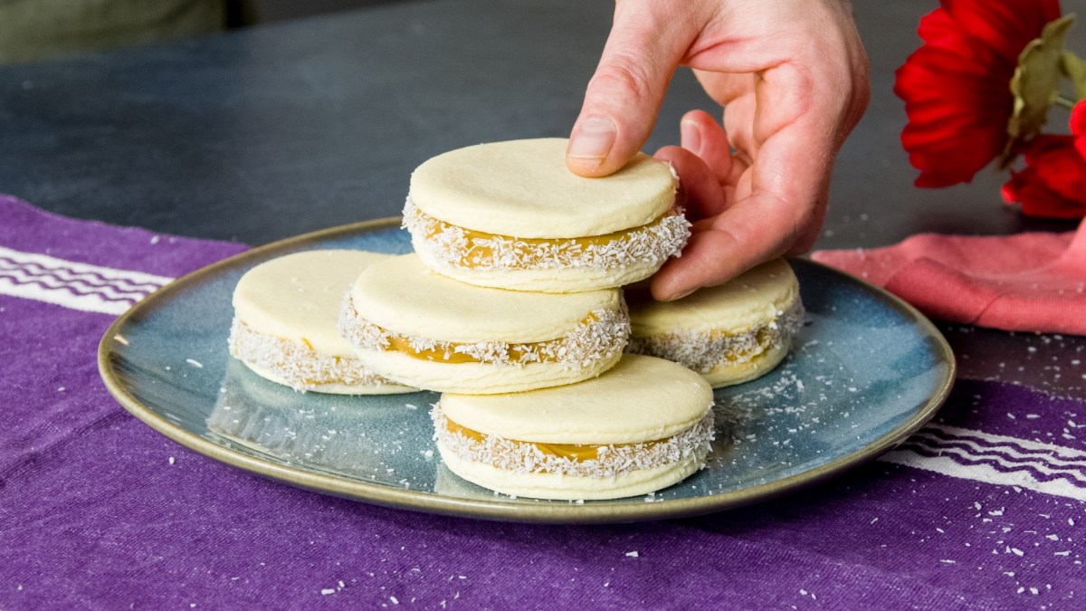Ein Stapel Alfajores auf einem Teller. Jemand nimmt sich den obersten Keks.