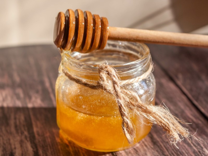 Ein Holzlöffel liegt auf einem Glas Honig.