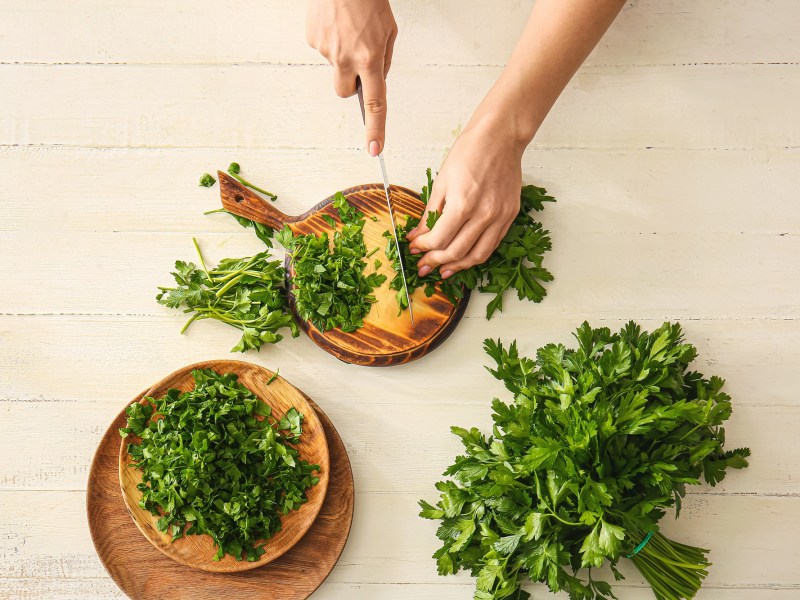 Eine Frau verwendet ein Messer und ein Holzbrett zum Kräuter schneiden.