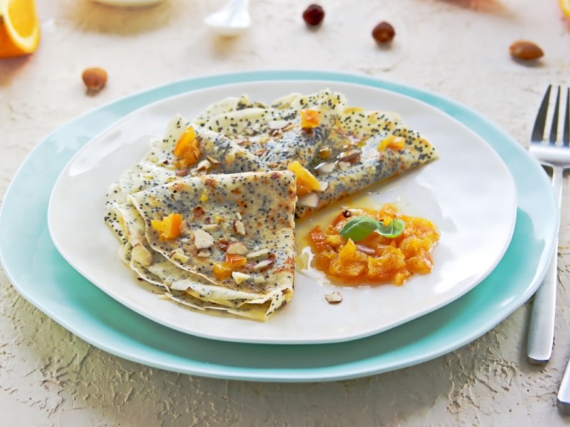 Mehrere Orangen-Mohn-Crêpes mit Haselnüssen auf einem Teller.