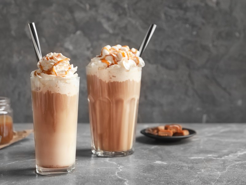 2 Gläser Salted Caramel Latte mit Schlagsahne, im Hintergrund Karamellbonbons.