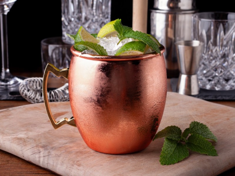 Ein Kupferbecher mit Virgin Moscow Mule. Barzubehör im Hintergrund.