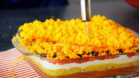 Seven-Layer-Dip: ein Koch schmilzt Cheddar mit einem Brenner.