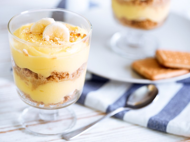 Ein Dessertglas mit Bananen-Buttercreme-Dessert. Im Hintergrund sieht man verschwommen ein weiteres Glas.