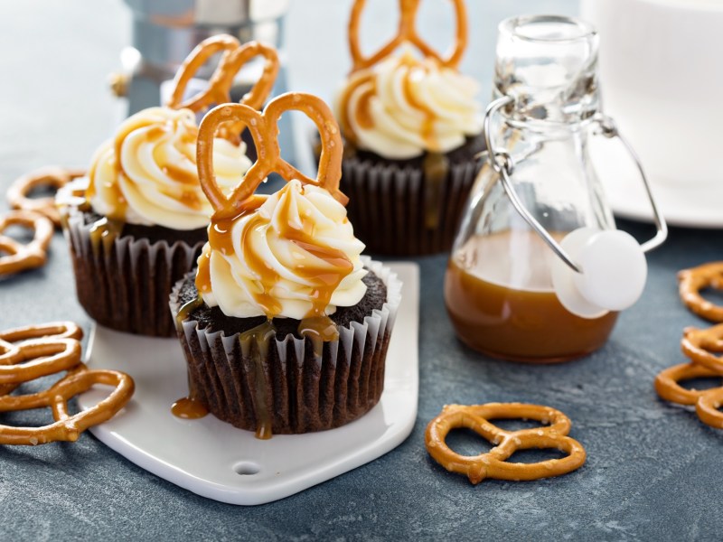 Brezel-Cupcakes auf einer UNterlage. Drum herum liegen kliene Salzbrezeln und eine Flasche mit Karamellsoße.