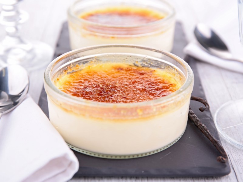 zwei Schalen Crème Brûlée mit Buttermilch auf einem Schieferbrett, daneben Servietten aus Stoff.