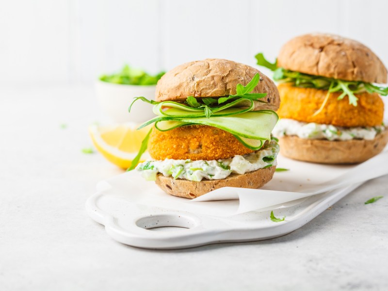 Zwei Fisch-Burger auf einem weißen Porzellantablett mit hellem Hintergrund.