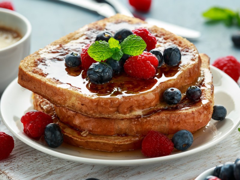 Ein Teller French Toasts aus der Heißluftfritteuse mit Beeren und Ahornsirup, Nahaufnahme.