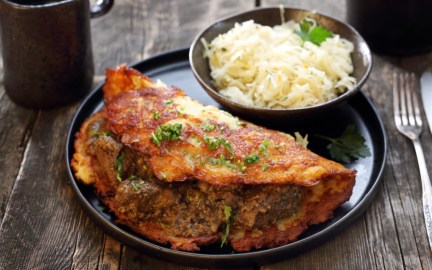 Ein Kartoffelpuffer mit Hackfleisch auf einem Teller. Daneben eine Schale mit Krautsalat.