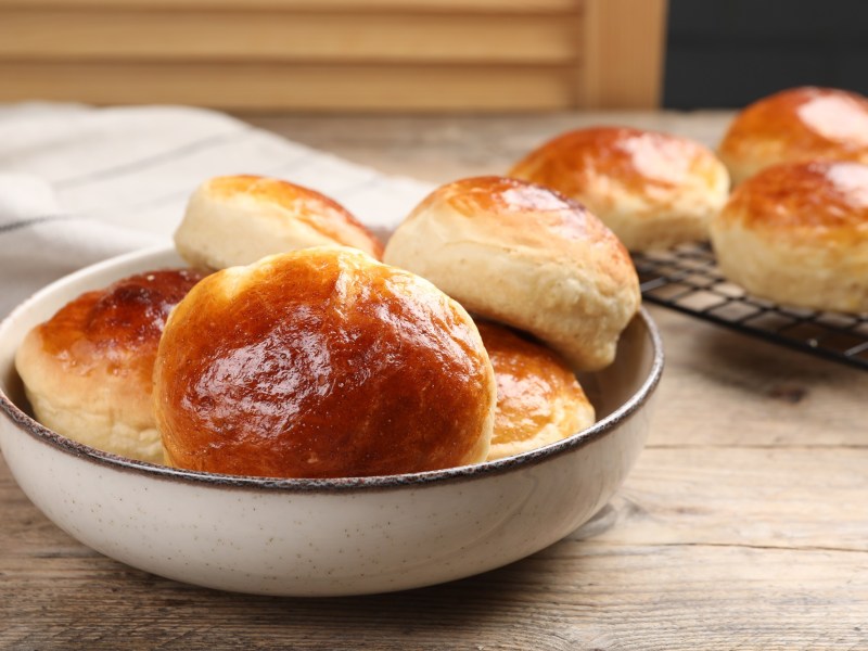 Marzipanbrötchen in einer Schale. Im Hintergrund liegen welche auf einem Abkühlgitter.