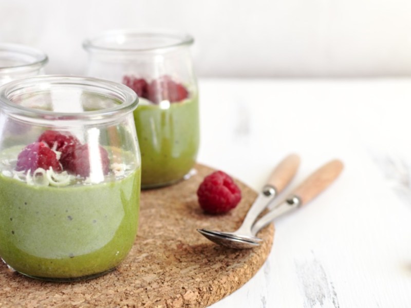 Drei Gläser Matcha-Pudding mit Himbeeren.