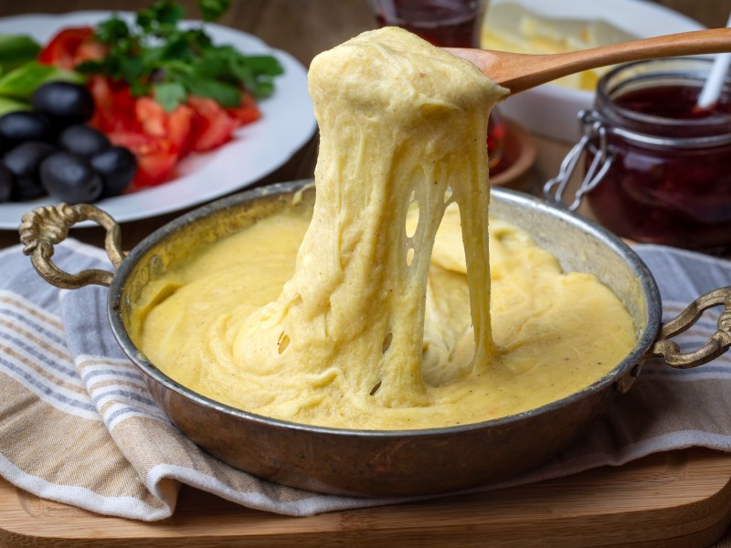 Ein Topf mit Mıhlama: türkisches Käsefondue. Ein Löffel zieht etwas von dem Fondue nach oben.