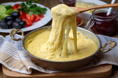 Ein Topf mit Mıhlama: türkisches Käsefondue. Ein Löffel zieht etwas von dem Fondue nach oben.