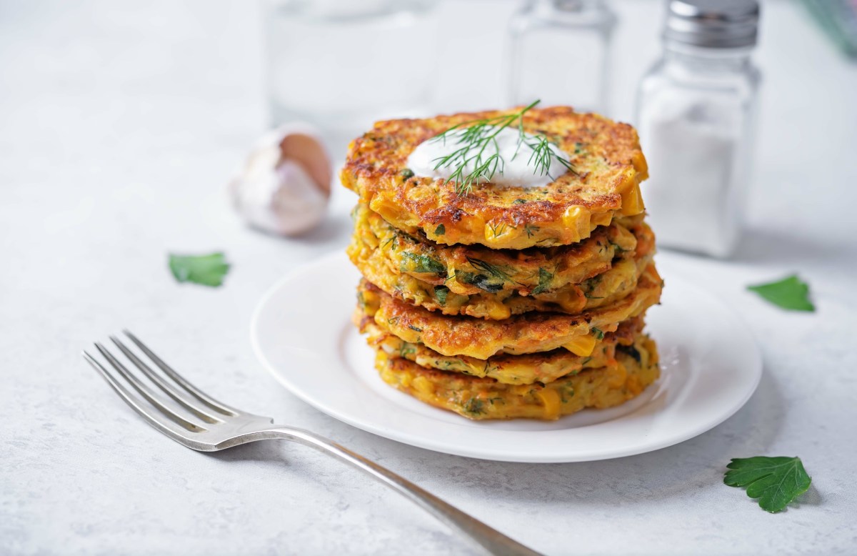 Ein Stapel Pastinaken-Möhren-Puffer mit Dill und Petersilie. Obendrauf ist ein Klecks Joghurts.