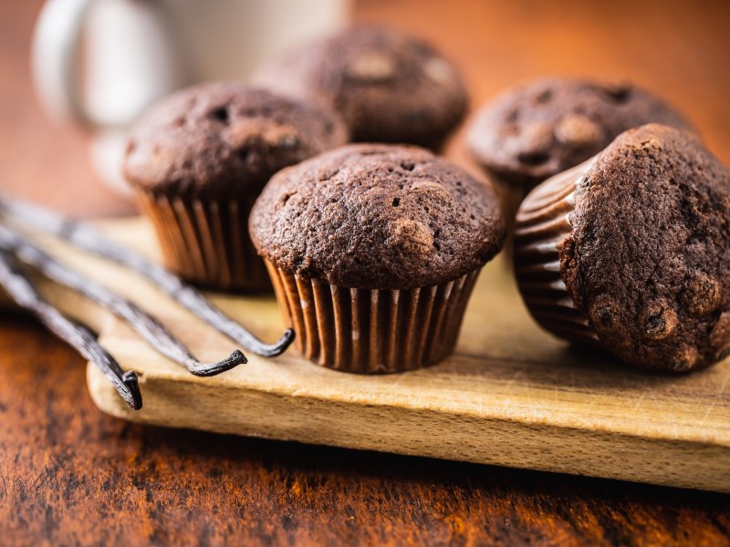 Ein paar Quark-Kakao-Muffins mit Schokolade auf einem Brett, daneben Vanilleschoten.