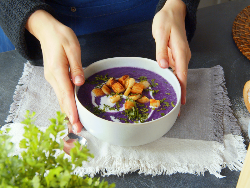 Eine Köchin präsentiert eine Schale mit lilafarbener Rotkohl-Kartoffel-Suppe.