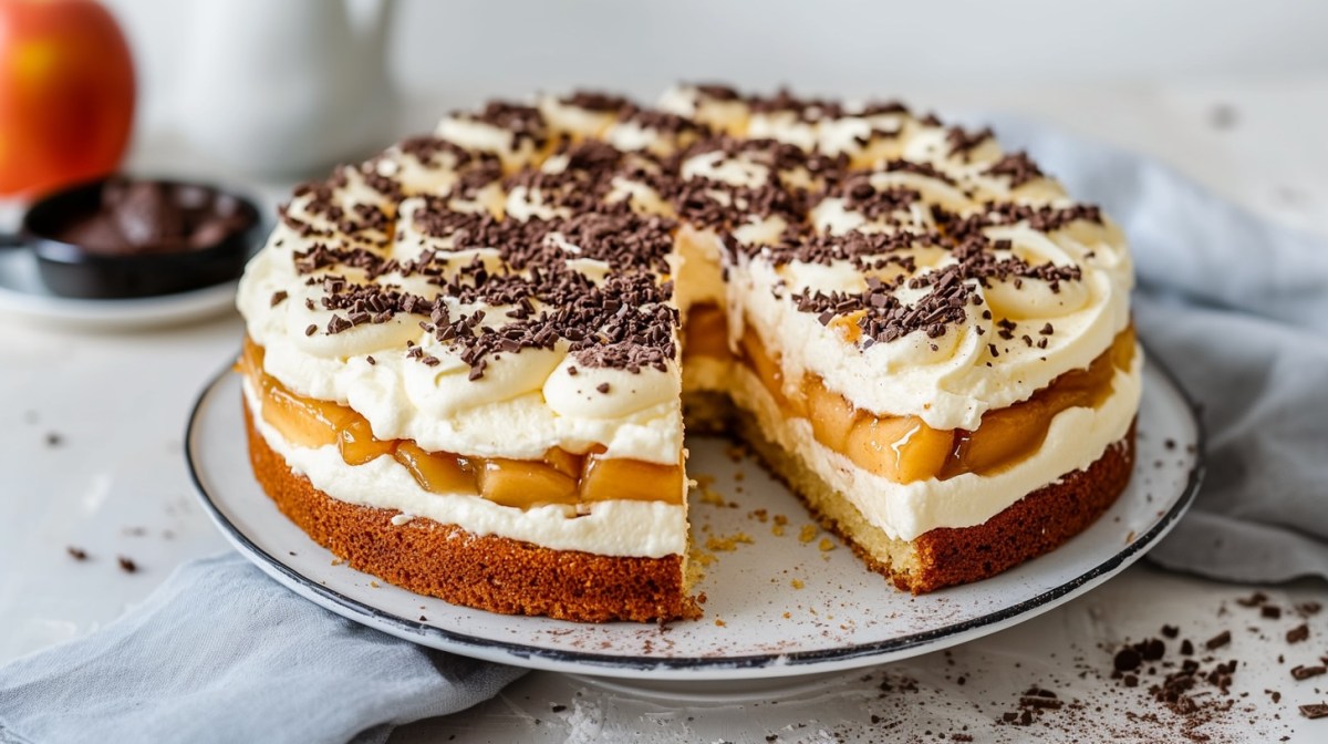 Eine angeschnittene schwedische Apfeltorte auf einem runden Teller, daneben eine Stoffserviette und gehackte Schokolade.