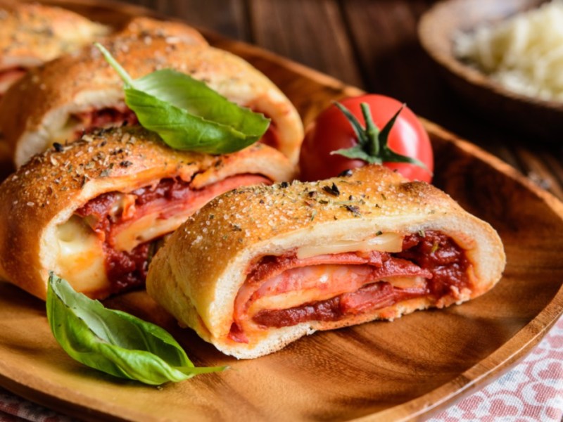 Stromboli Pizza mit Salami und Käse auf einem Holztablett.