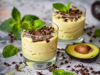 Zwei Gläser Avocado-Minz-Creme mit aufgeschnittener Avocado und Minze daneben