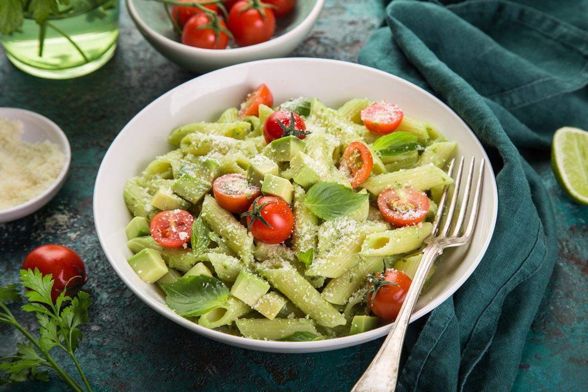 Avocado-Nudelsalat in einem tiefen Teller, serviert mit Parmesan und Tomaten.