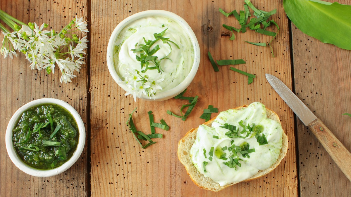 Glas und Stulle mit Bärlauchaufstrich samt Messer auf Holz-Untergrund.