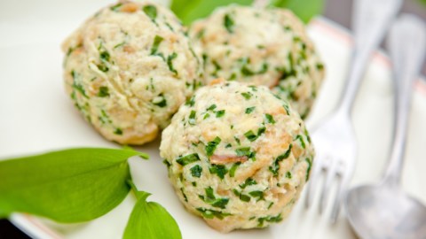 Drei Bärlauchknödel auf einem Teller. Daneben liegen Besteck und frischer Bärlauch.