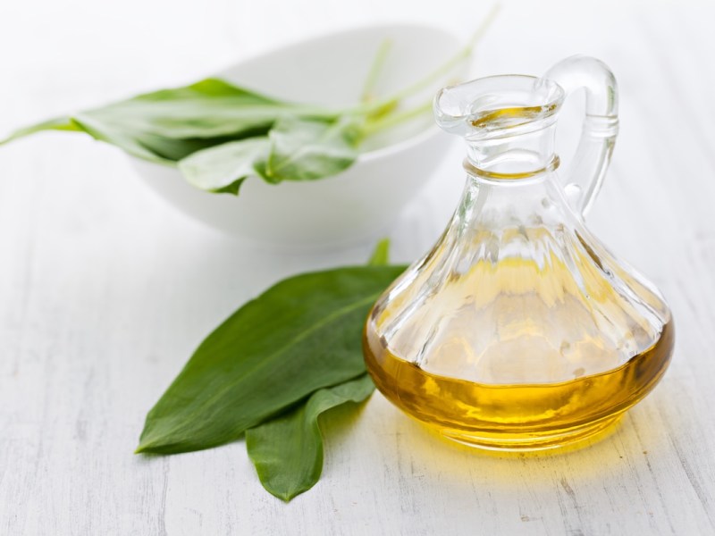 Eine Flasche Bärlauchöl, daneben einige Bärlauchblätter.