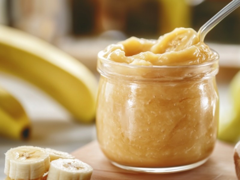 Ein Glas Bananengelee. Drumherum sind Bananen zu sehen.