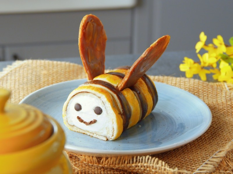 Eine süße Bienenstichrolle in Bienenform auf einem Teller.