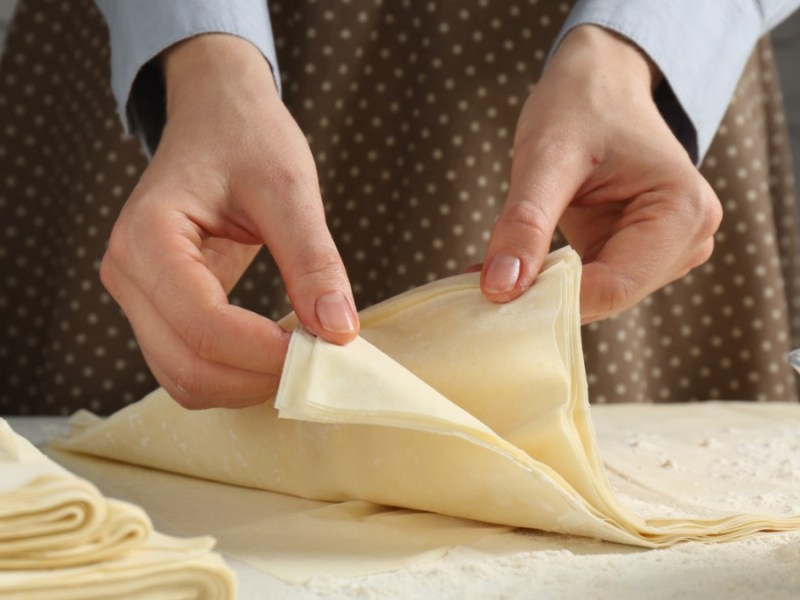 Tipps fürs Backen mit Blätterteig: Eine Frau zieht mehrere, übereinander gelegte Blätterteige mit den Händen auseinander.
